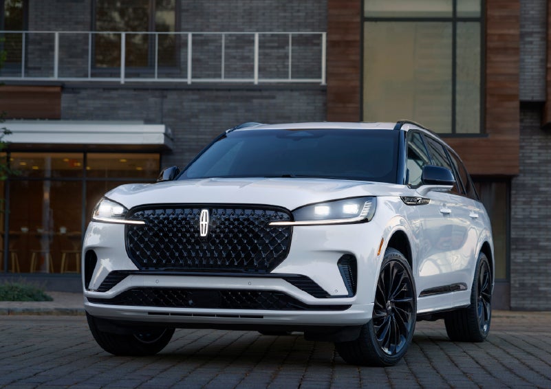 A 2026 Lincoln Aviator® Reserve model is shown with the available Jet Appearance Package parked near a restaurant. | Lincoln of Troy in Troy MI