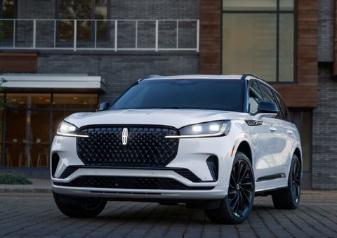 A 2026 Lincoln Aviator® Reserve model is shown with the available Jet Appearance Package parked near a restaurant. | Lincoln of Troy in Troy MI