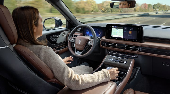 A 2026 Lincoln Aviator® SUV is being driven hands-free on a highway near a forest | Lincoln of Troy in Troy MI