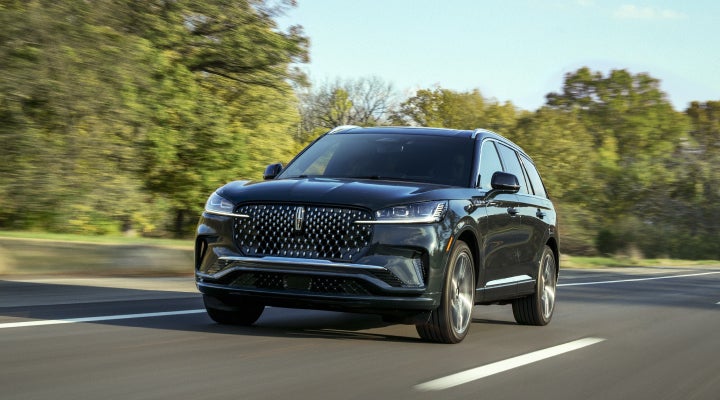A 2026 Lincoln Black Label™ Aviator® SUV is being driven down a road lined with trees. | Lincoln of Troy in Troy MI