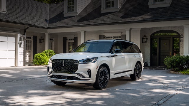 A white 2026 Lincoln Aviator® SUV is parked in the driveway of a luxury home. | Lincoln of Troy in Troy MI