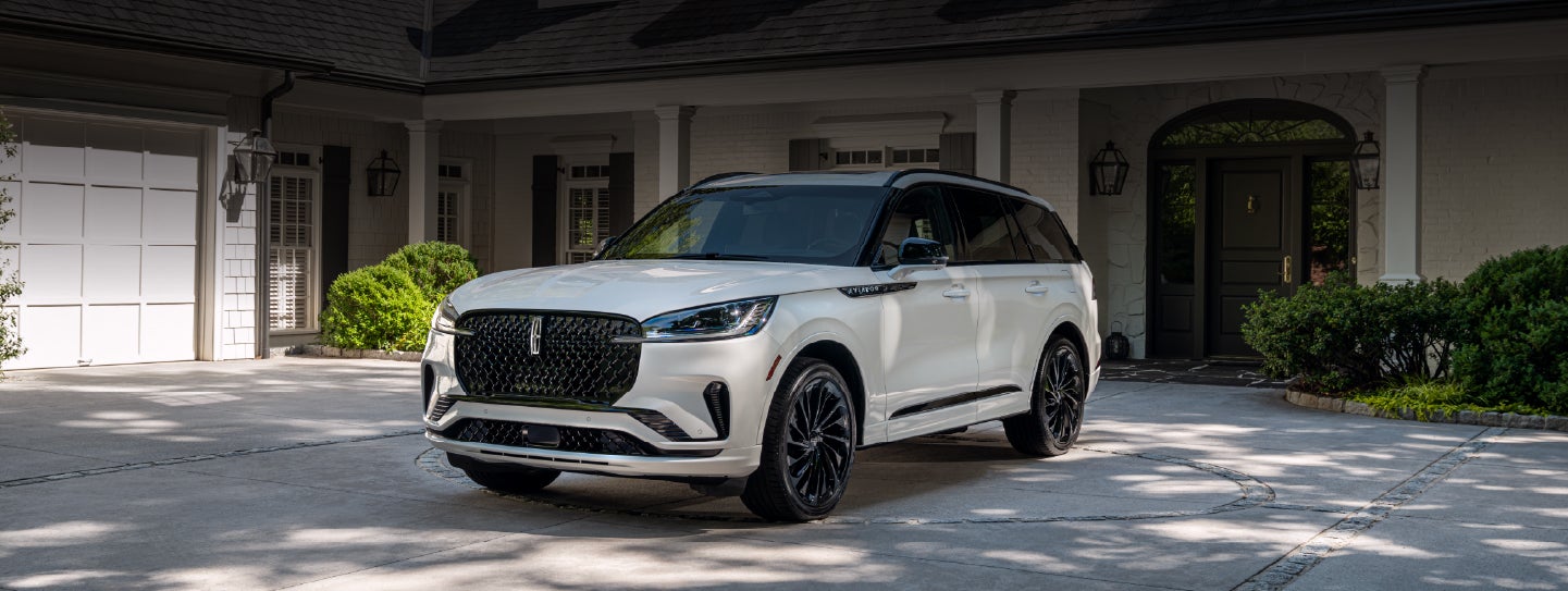 A white 2026 Lincoln Aviator® SUV is parked in the driveway of a luxury home. | Lincoln of Troy in Troy MI