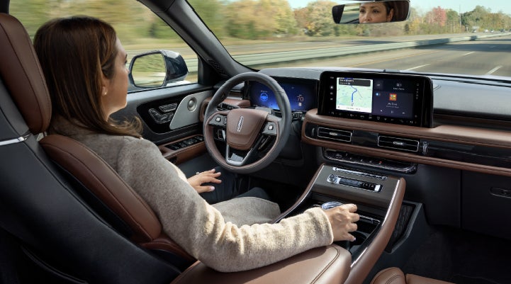 A 2027 Lincoln Aviator® SUV is being driven hands-free on a highway lined with trees. | Lincoln of Troy in Troy MI