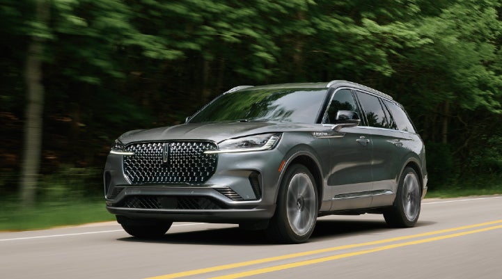 A 2027 Lincoln Aviator® SUV is being driven down a road lined with trees. | Lincoln of Troy in Troy MI