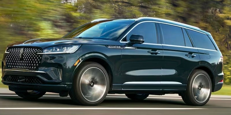 Dark-colored SUV driving on a road with motion-blurred trees and greenery in the background