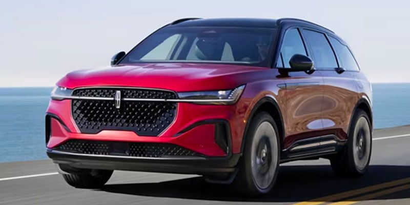 Red Lincoln SUV driving on a coastal roadway, shown from a front three-quarter angle