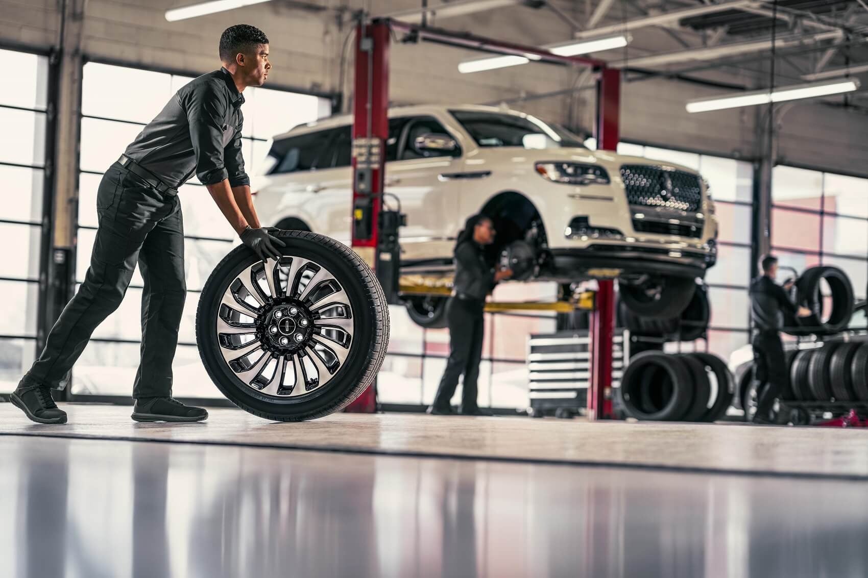 service tech rolling new tires to vehicle in service