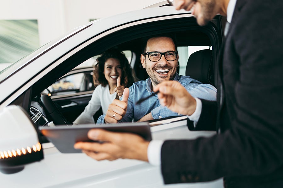 Vehicle customer seated in a car giving a thumbs-up while reviewing documents