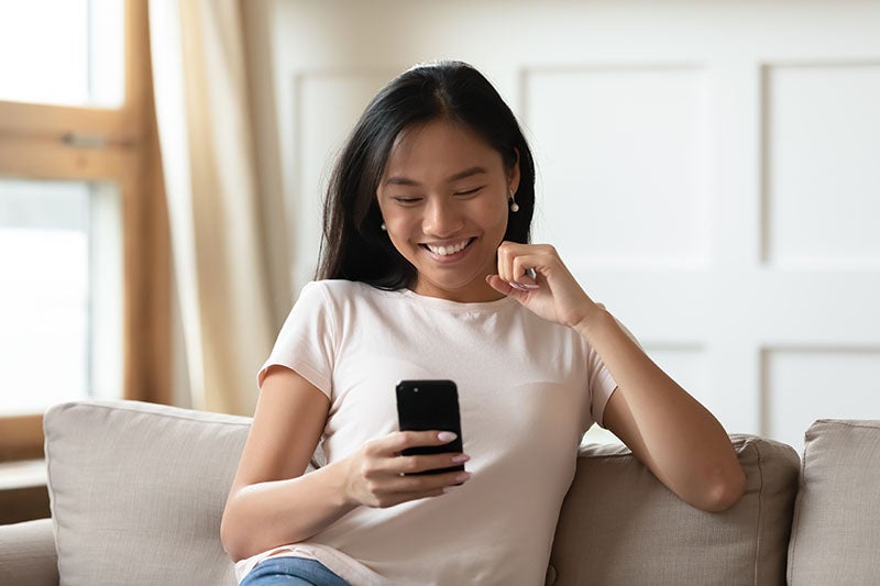 Person sitting on a light-colored sofa and looking at a smartphone in a bright living room
