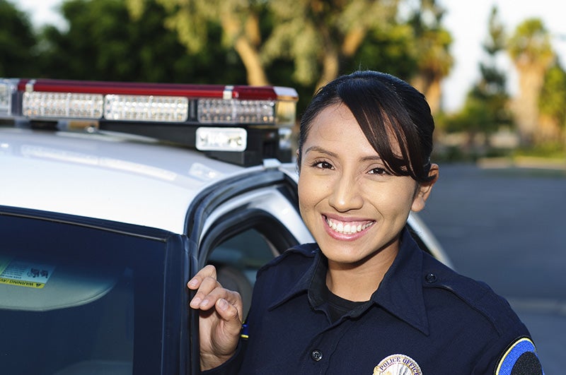 Uniformed police officer standing beside a patrol vehicle with emergency lights visible on the roof