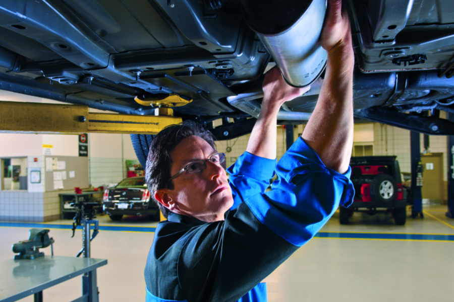 Mechanic in glasses and uniform working on a car's exhaust system, suspended on a lift in a garage