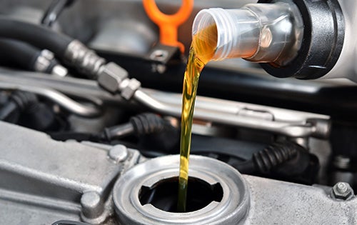 Motor oil being poured from a plastic container into the engine oil fill opening of a vehicle engine during a routine oil service