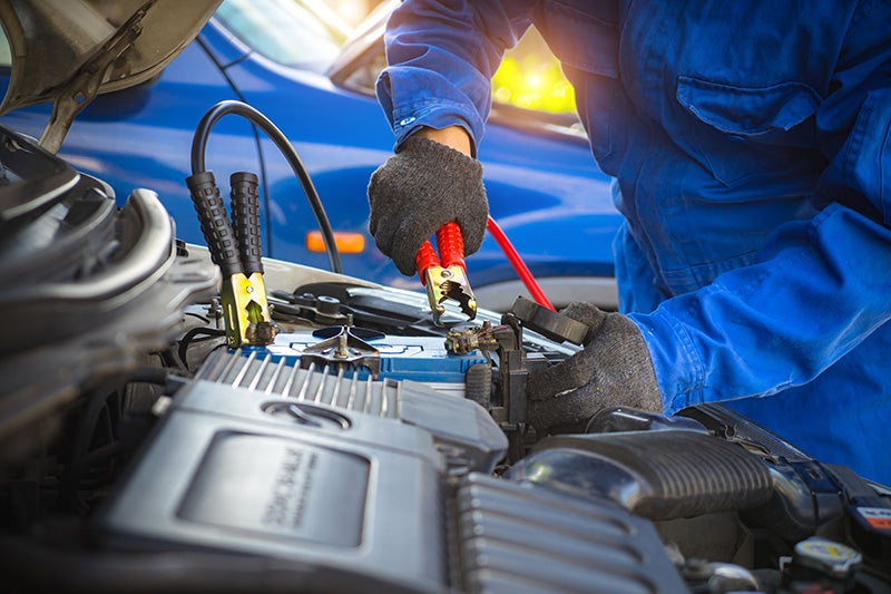 Close-up of a technician connecting jumper cables to a car battery in an engine compartment