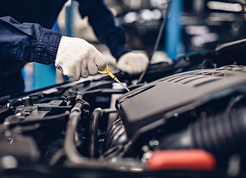 A gloved hand dips a yellow dipstick into a car engine to check the oil level