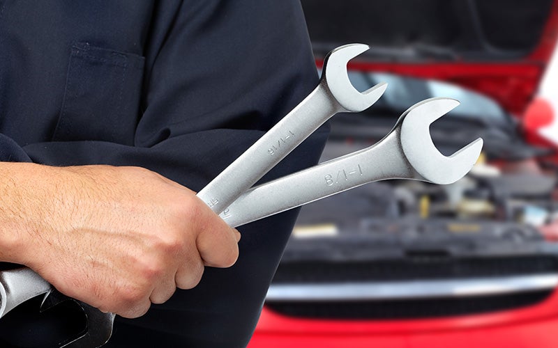 Close-up of a person holding two wrenches in an automotive repair shop